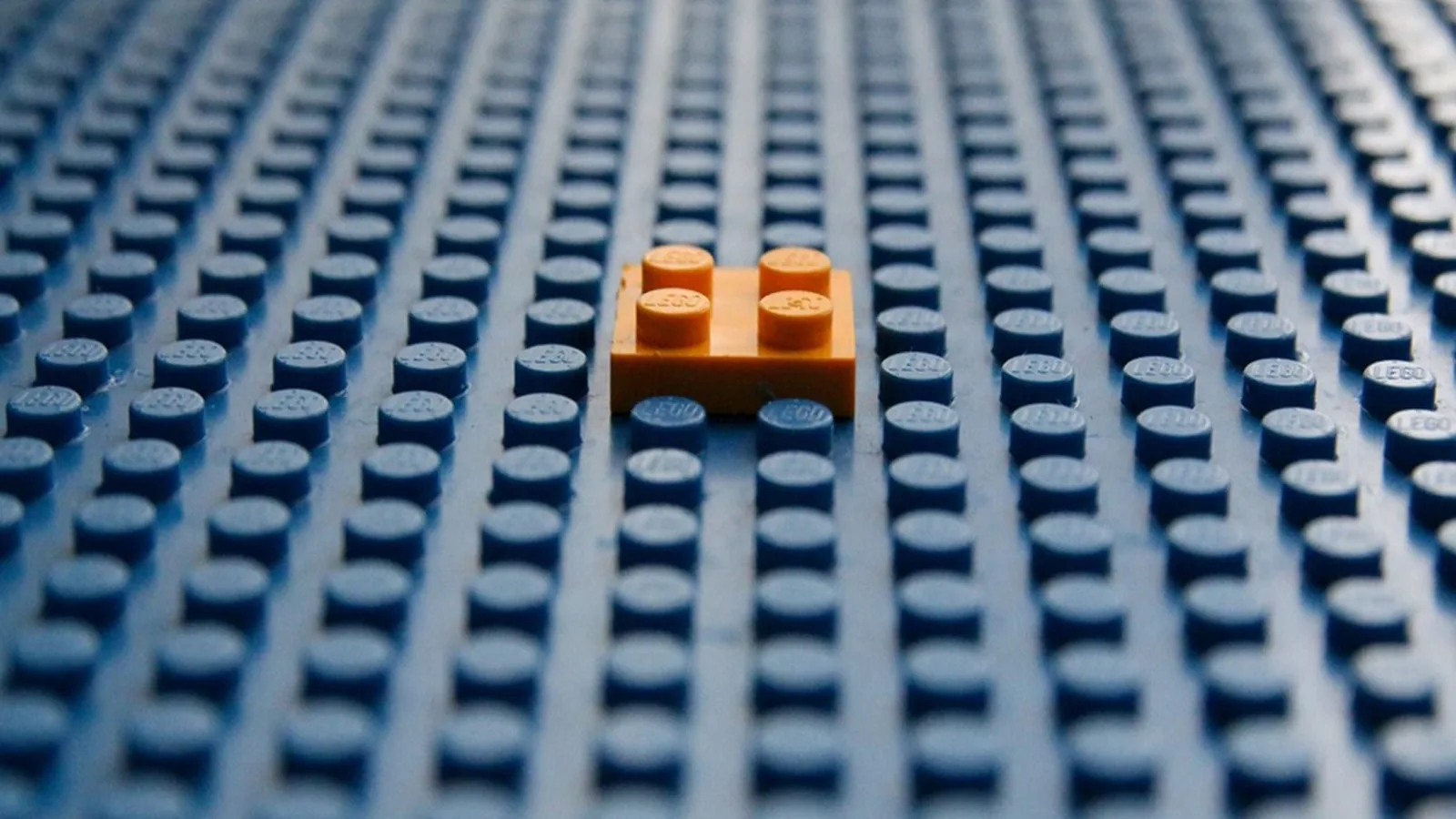 Синяя пластина Lego, сплошь усыпанная одинаковыми пупырышками, и одна оранжевая деталь на два на два в центре