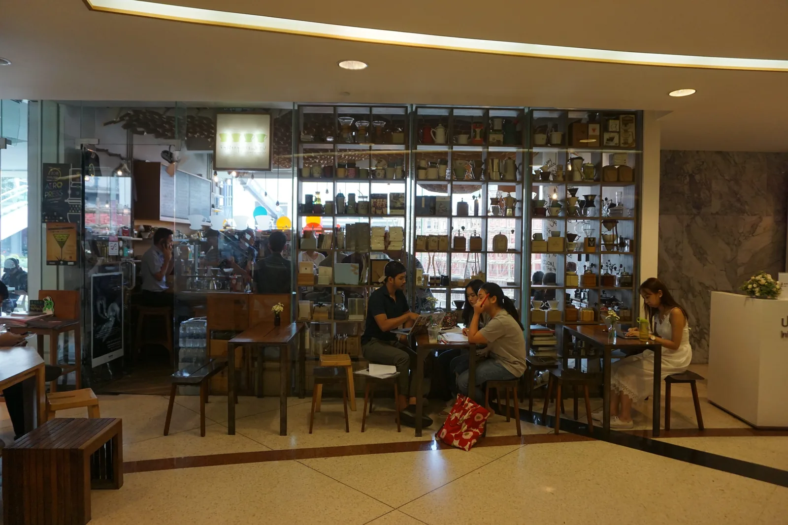 The coffee shop seen from the entrance: bar stools, a long table and a wall of shelves