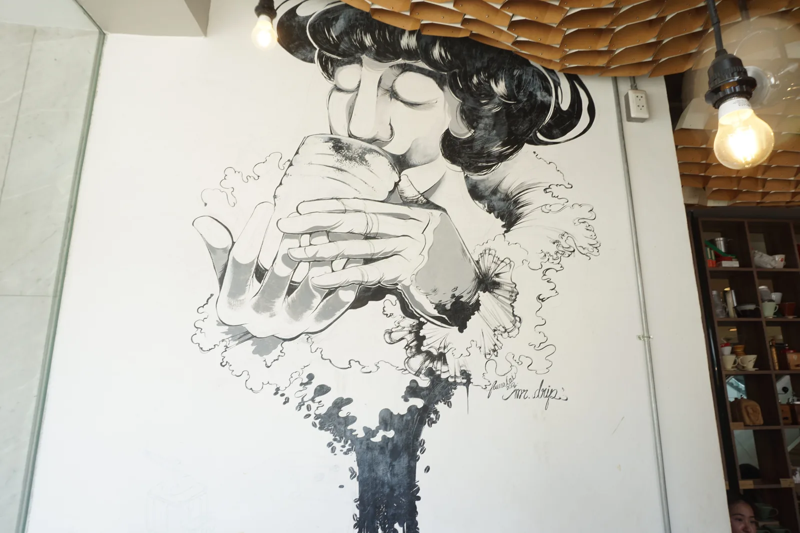 A wall drawing of a woman drinking from a cup, coffee beans pouring out of it