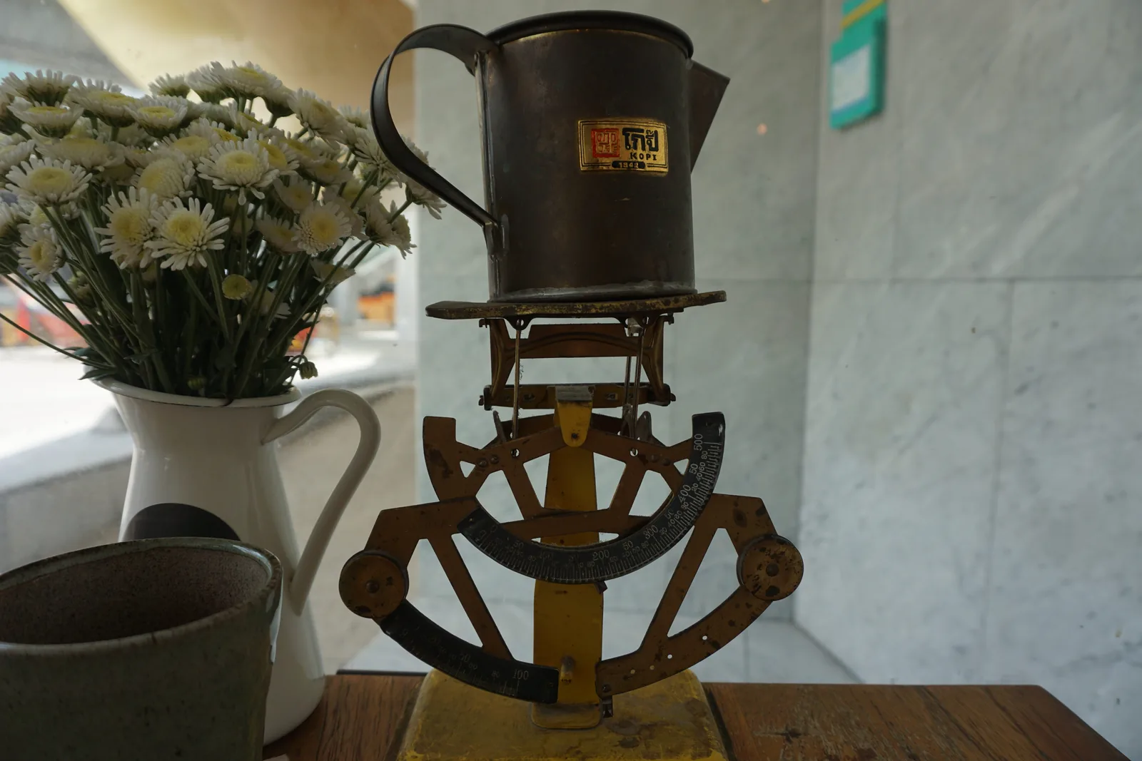 A copper pour-over kettle on a stand beside a jug of daisies