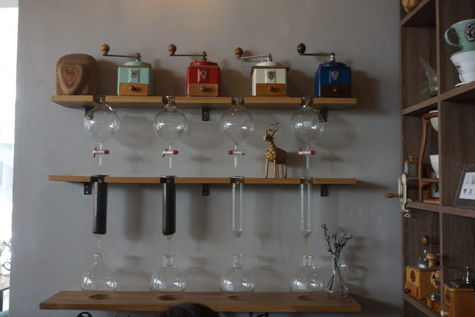 Hand grinders lined up on a shelf above siphon brewers