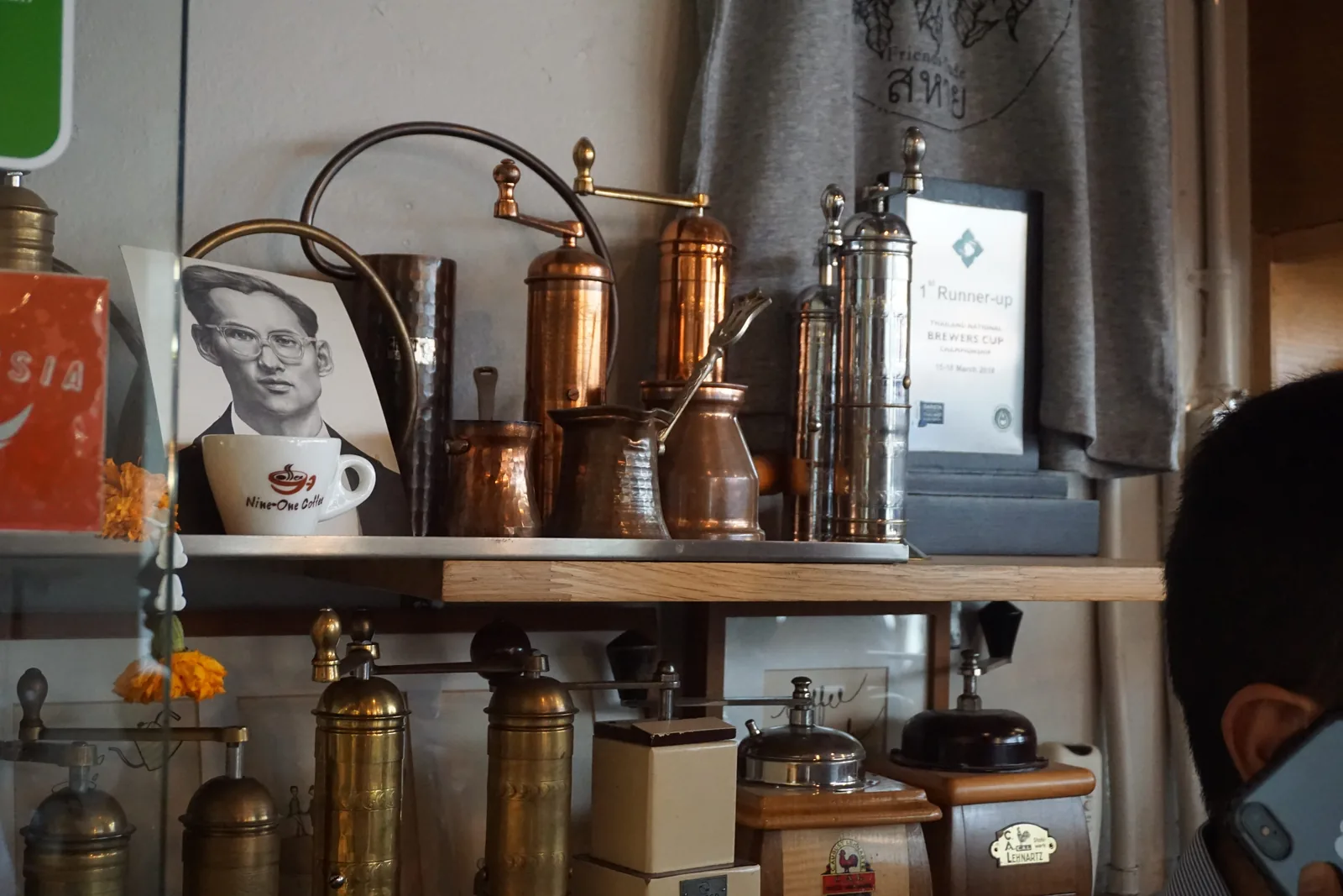 A shelf of copper grinders and brewing gear behind a framed portrait