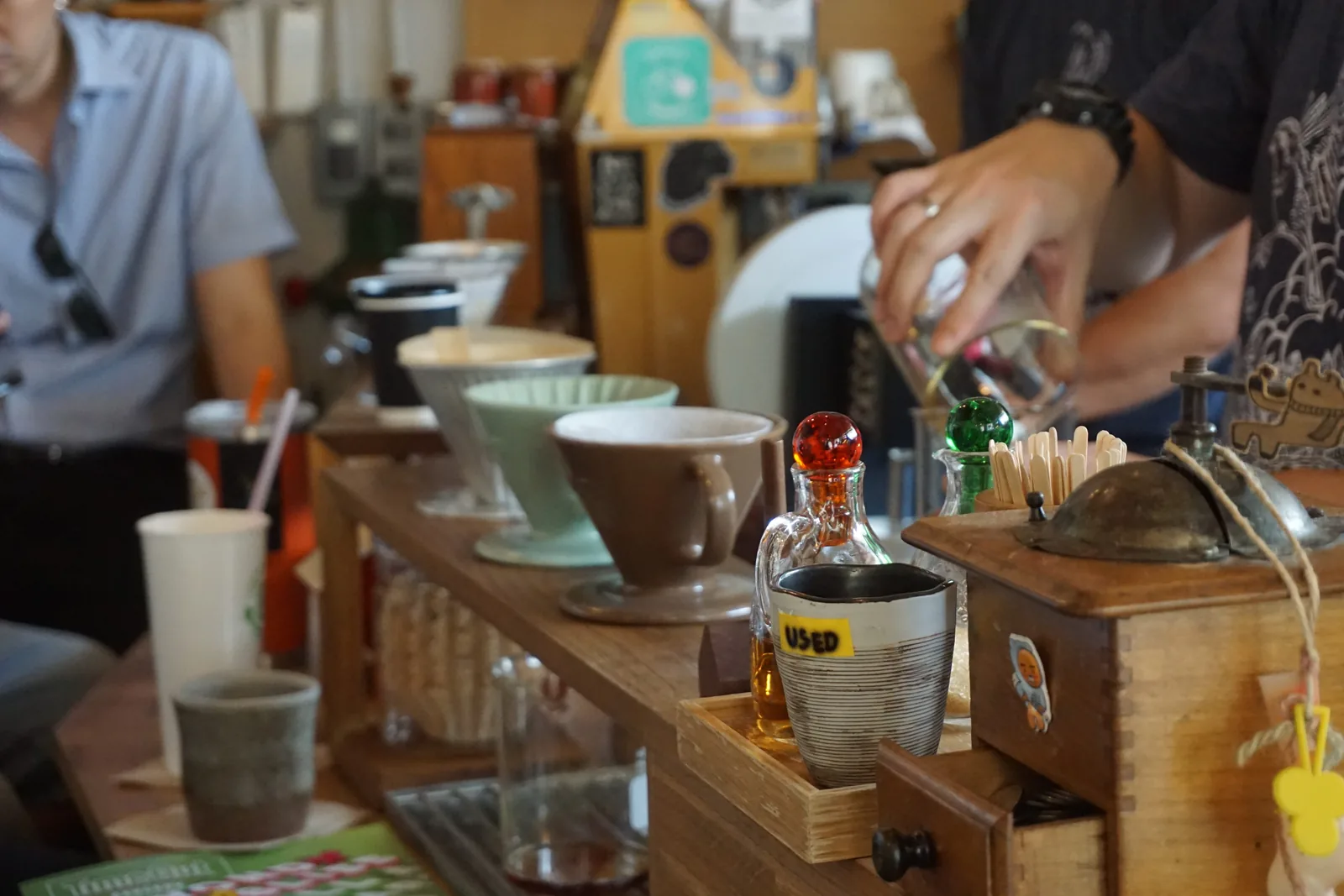 A barista pouring water over a filter at a counter lined with siphons