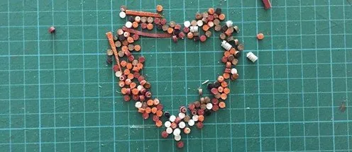 Обрезки кожи и фурнитура, выложенные в форме сердца на зелёном раскройном мате