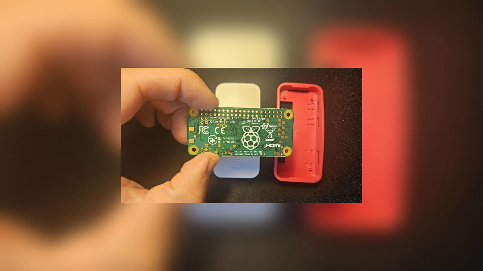 A Raspberry Pi Zero board held between two fingers above its cases