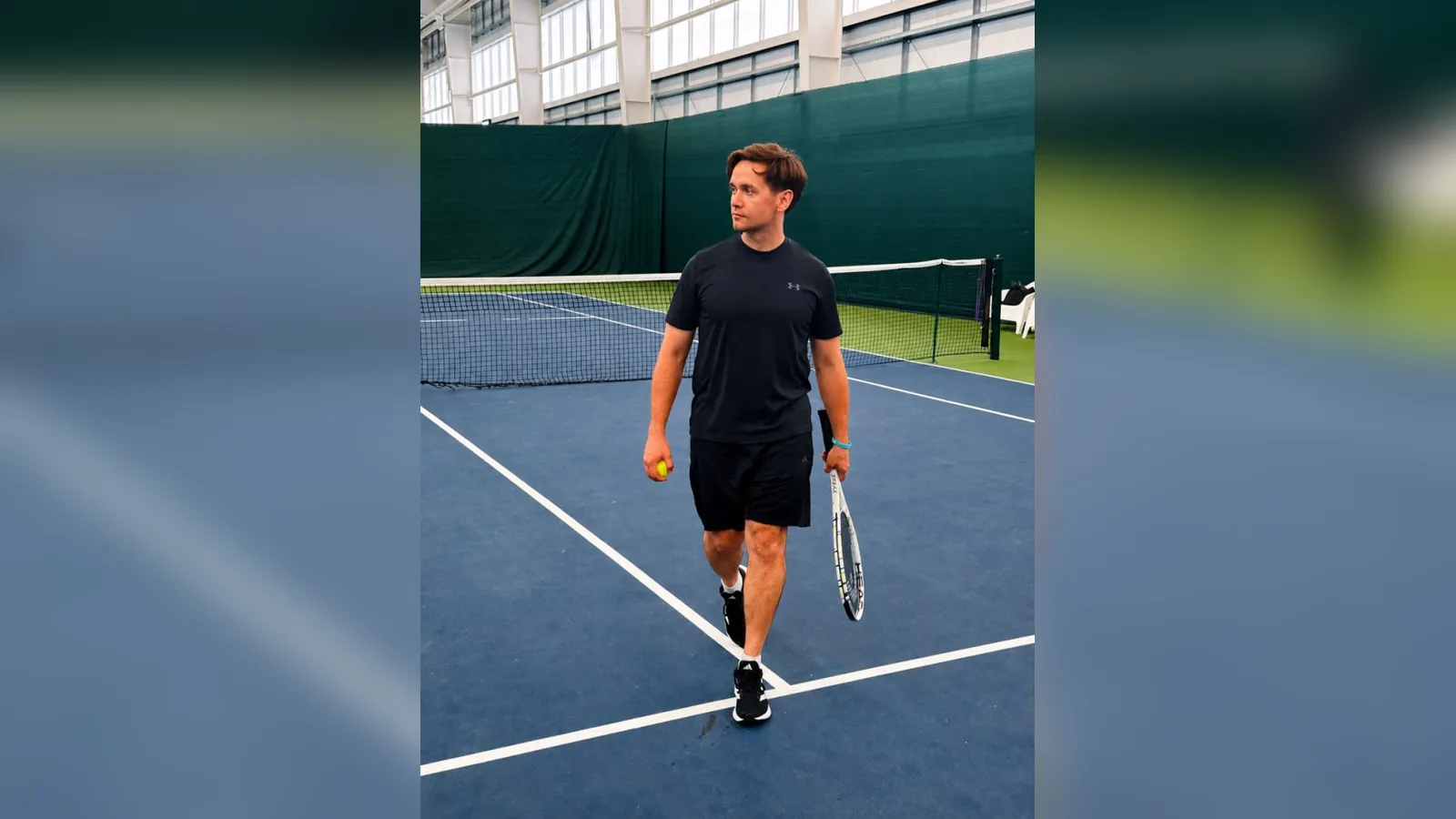Maksim walking across a tennis court holding a racket