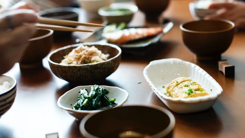 Small bowls of food on a wooden table with chopsticks resting over one of them